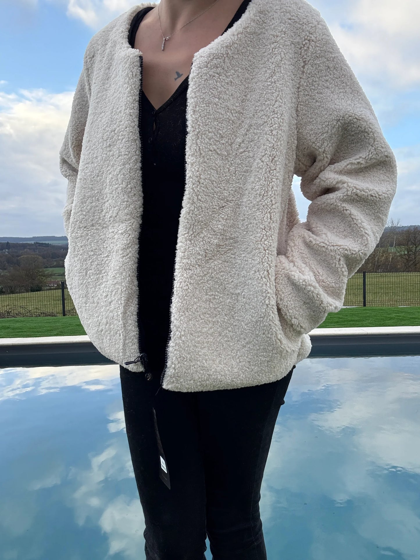 Veste courte réversible femme Laura Jo côté sherpa beige portée ouverte avec manches bouffantes, devant piscine