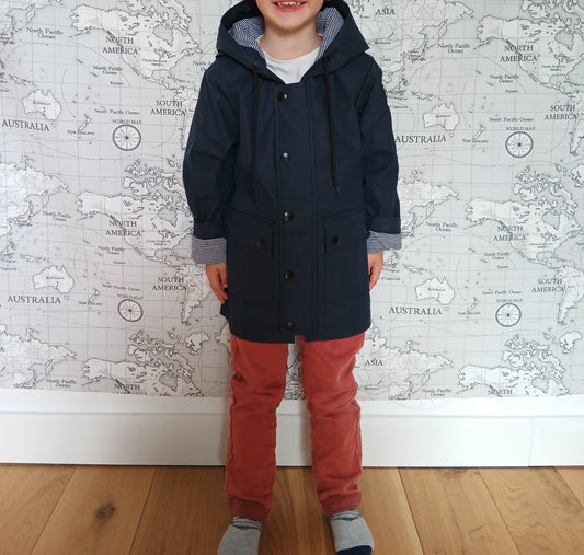 Child wearing navy raincoat with striped lining, standing in front of world map wallpaper