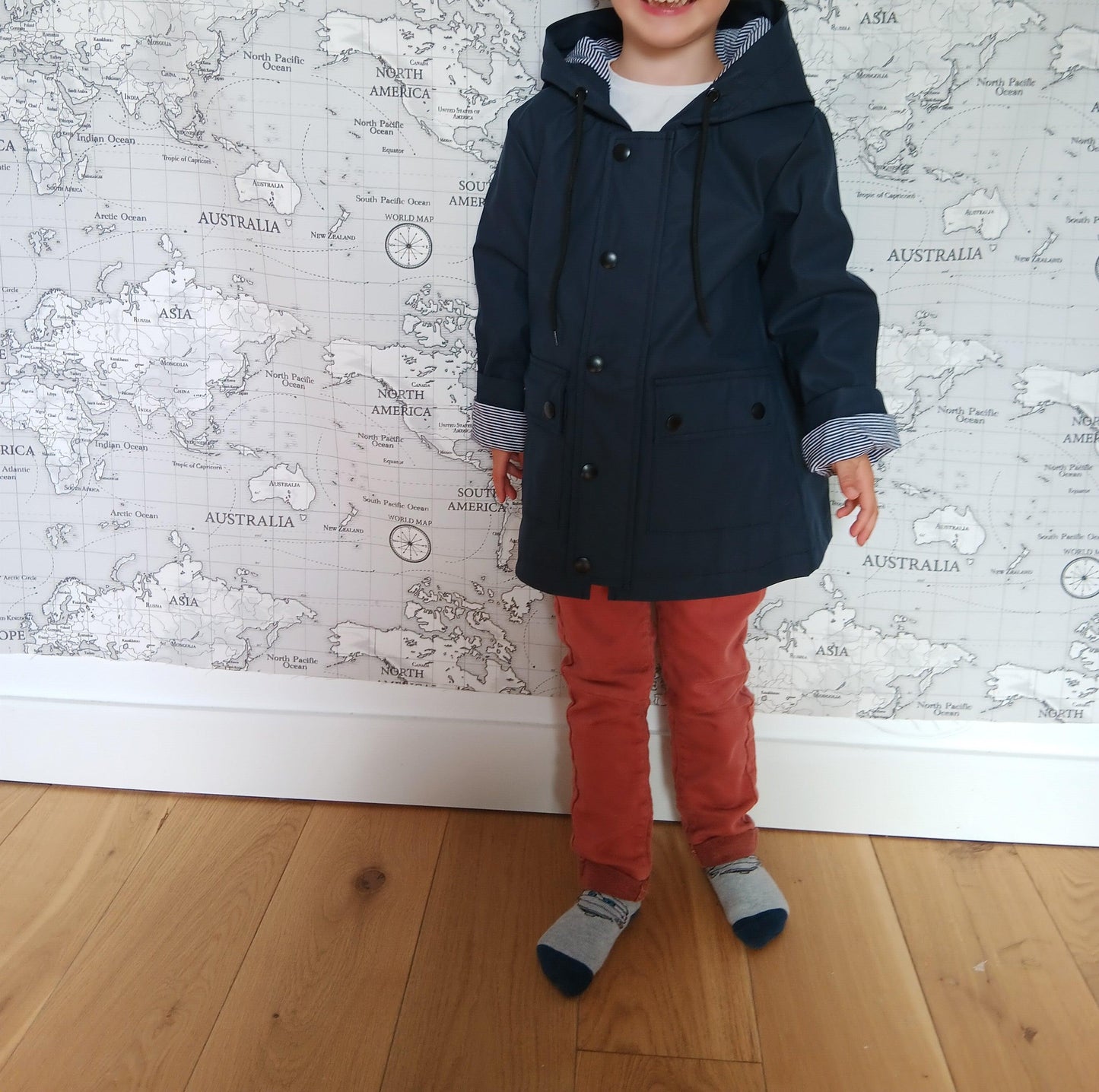 Child wearing navy raincoat with cotton lining and red pants in front of world map wall