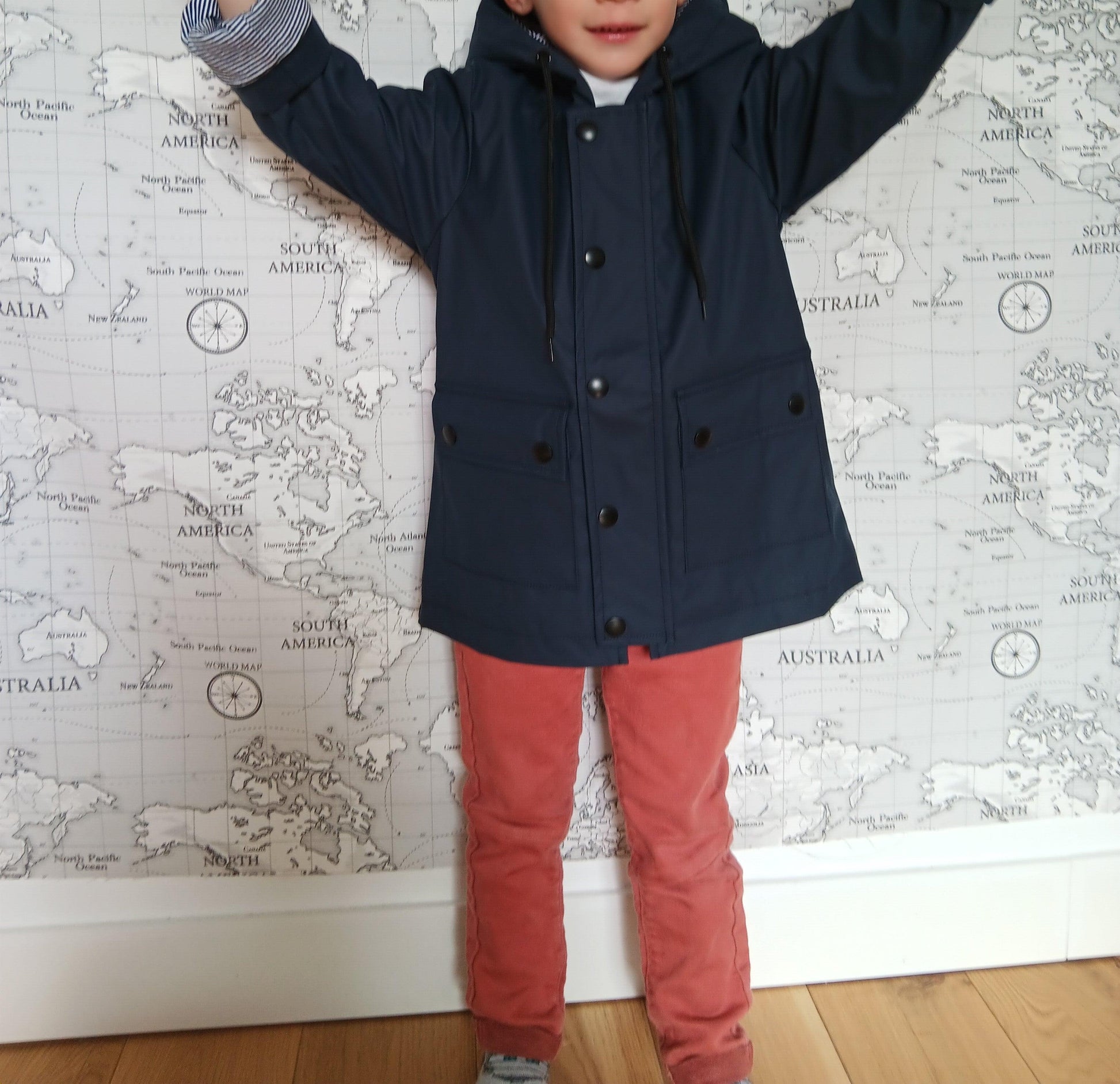 Child wearing navy blue Laura Jo raincoat, standing indoors by world map wallpaper