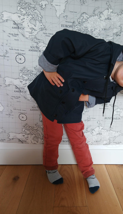 Child in navy blue raincoat and red pants posing in front of world map wall, Le Petit Placard