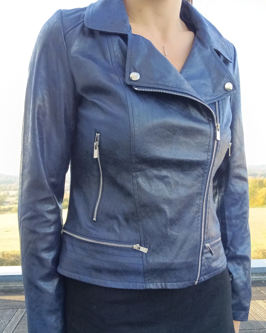 Woman wearing a navy blue faux leather biker jacket from Le Petit Placard, outdoor setting