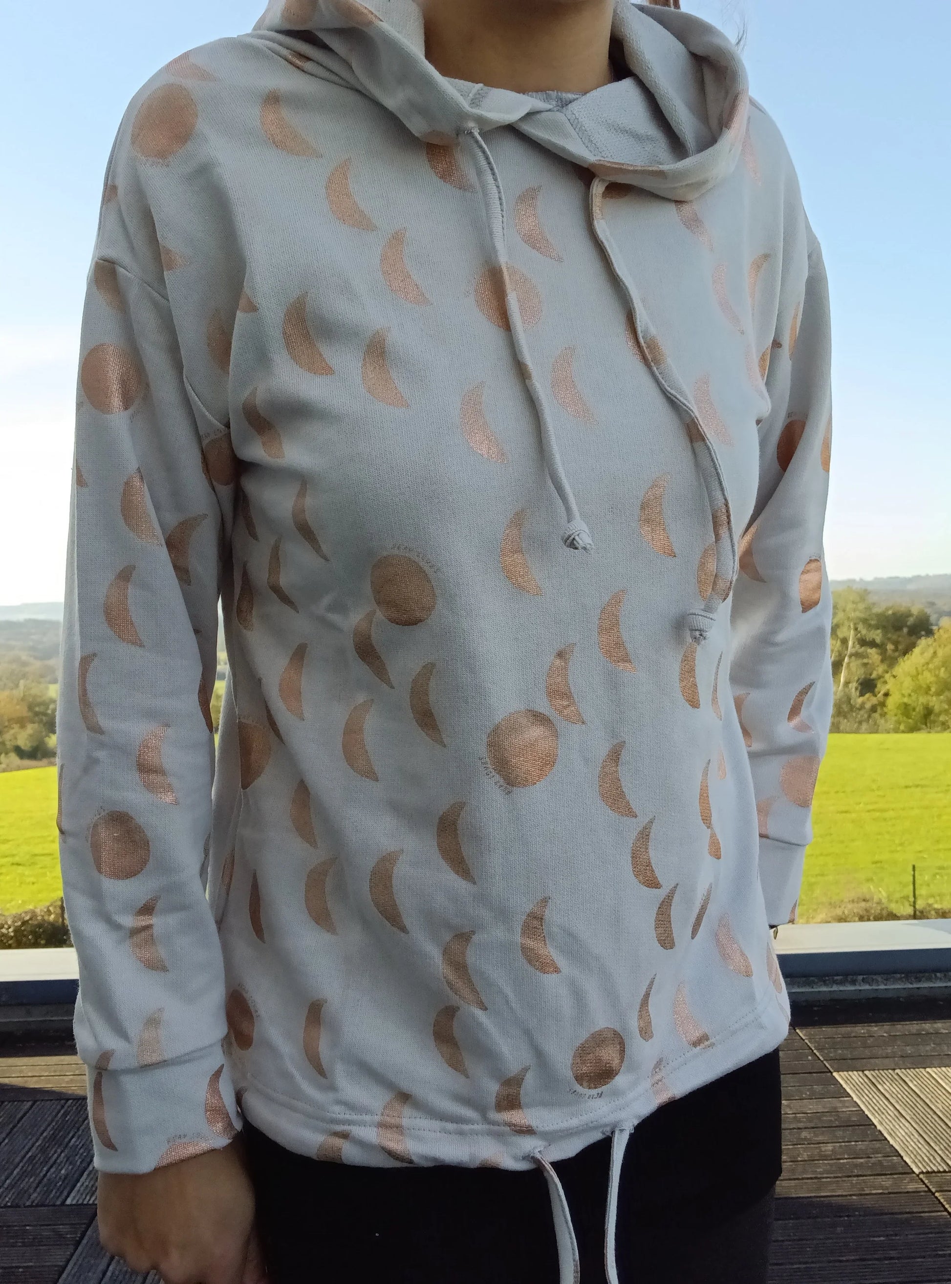Sweat à capuche blanc crème avec cordon, imprimé de motifs lune doré rosé, porté par une femme
