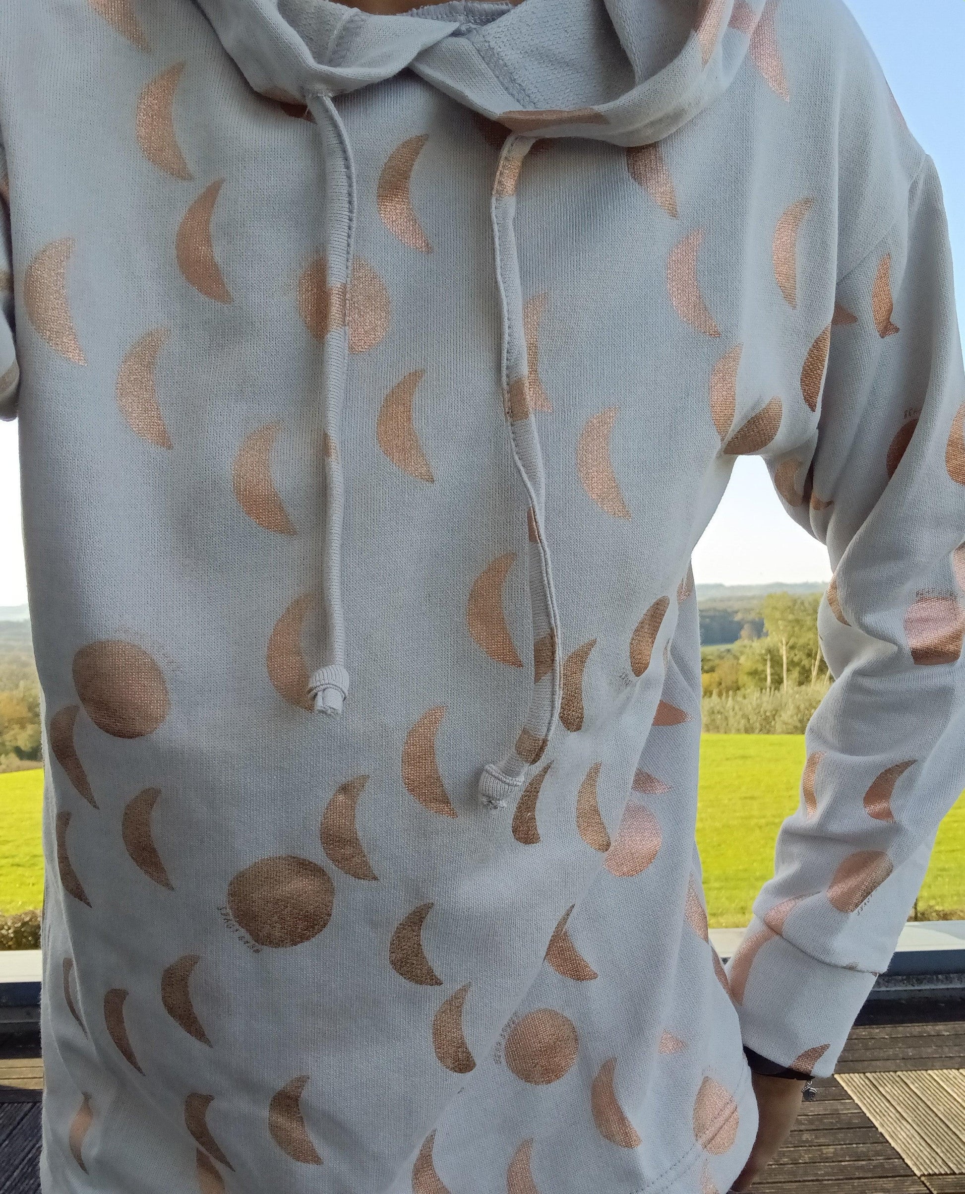Sweat à capuche blanc crème avec cordon et motifs lune doré rosé brillant, porté en extérieur