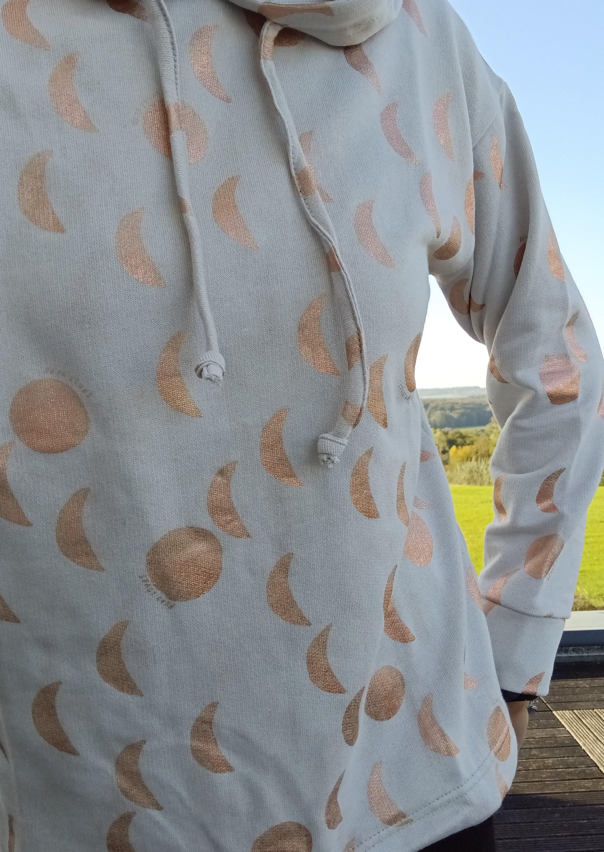 Sweat à capuche blanc crème avec cordon et motifs lune doré rosé, porté en extérieur