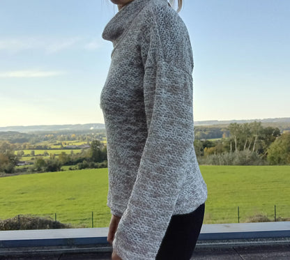 Pull col montant à grosses mailles beige taupe porté de profil par une femme, vue sur campagne verdoyante