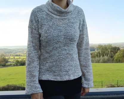 Pull col montant à grosses mailles beige taupe porté par une femme devant un paysage verdoyant
