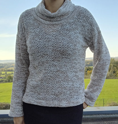 Pull col montant à grosses mailles beige taupe porté par une femme, fond de campagne verdoyante