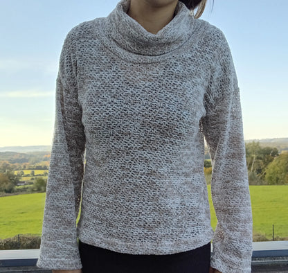 Pull col montant à grosses mailles beige taupe porté par une femme devant un paysage verdoyant