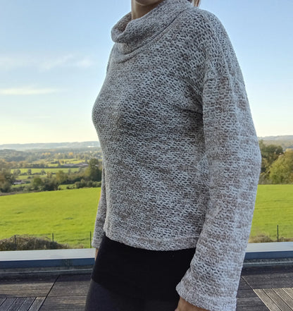 Pull col montant à grosses mailles beige taupe porté de profil, vue extérieure avec paysage verdoyant
