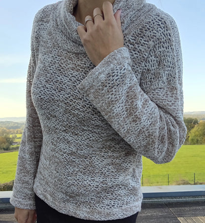 Pull col montant grosses mailles beige taupe porté par une femme, fond de campagne verdoyante