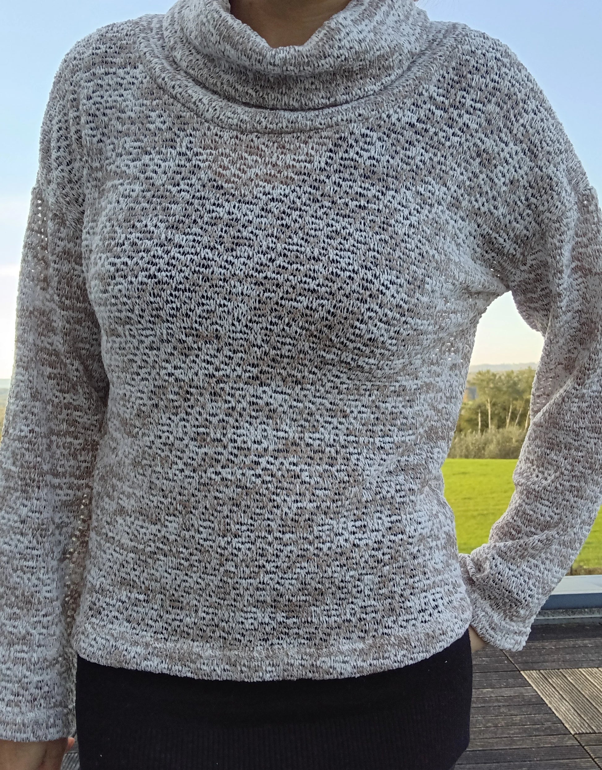 Pull col montant à grosses mailles beige taupe porté par une femme, fond de jardin en extérieur