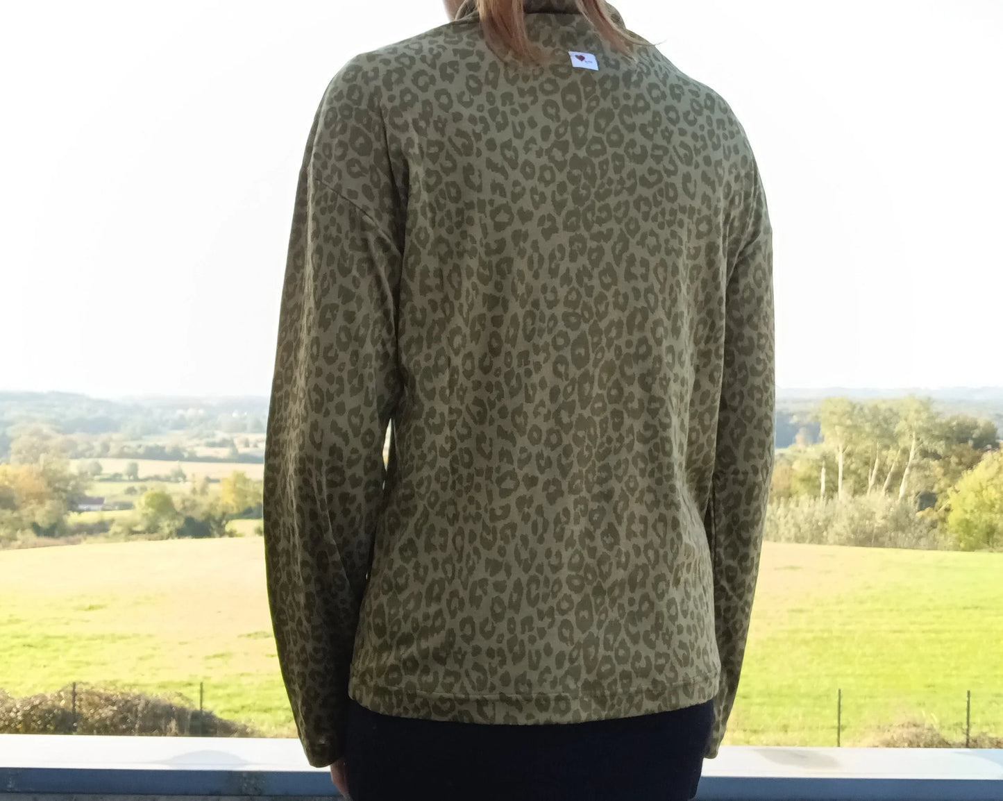 Vue de dos d'un pull fin col montant motifs léopard kaki porté par une femme devant un paysage verdoyant