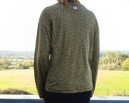 Vue de dos d'un pull fin col montant motifs léopard kaki porté par une femme devant un paysage verdoyant