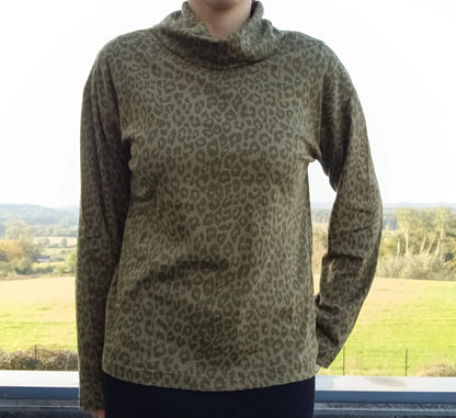 Pull fin à col montant motifs léopard kaki porté par une femme, fond paysage verdoyant