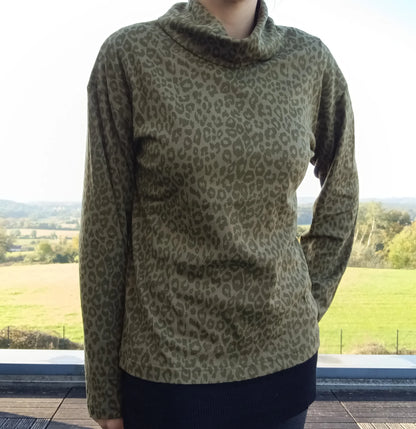 Pull fin à col montant motifs léopard kaki porté par une femme, fond paysage verdoyant