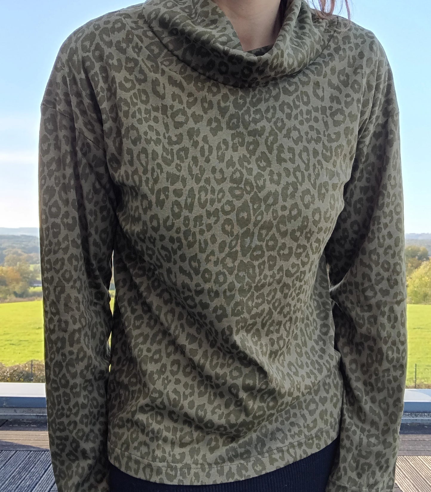 Pull fin à col montant motifs léopard kaki porté par une femme, fond de campagne verdoyante