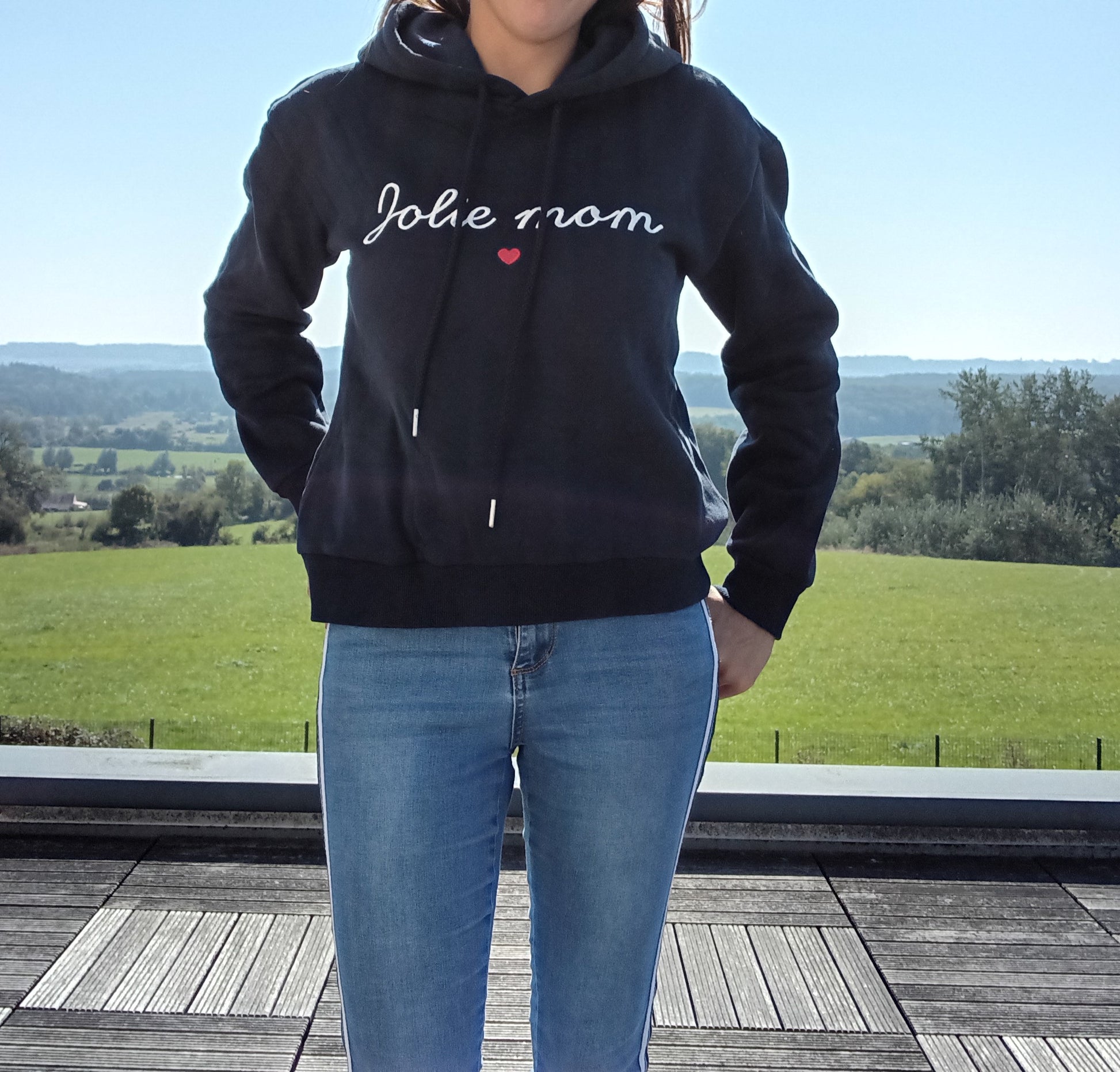 Woman wearing black 'Jolie mom' hoodie and blue jeans outdoors, Le Petit Placard fashion