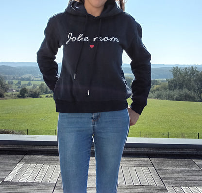 Woman wearing black 'Jolie mom' hoodie and blue jeans outdoors, Le Petit Placard fashion