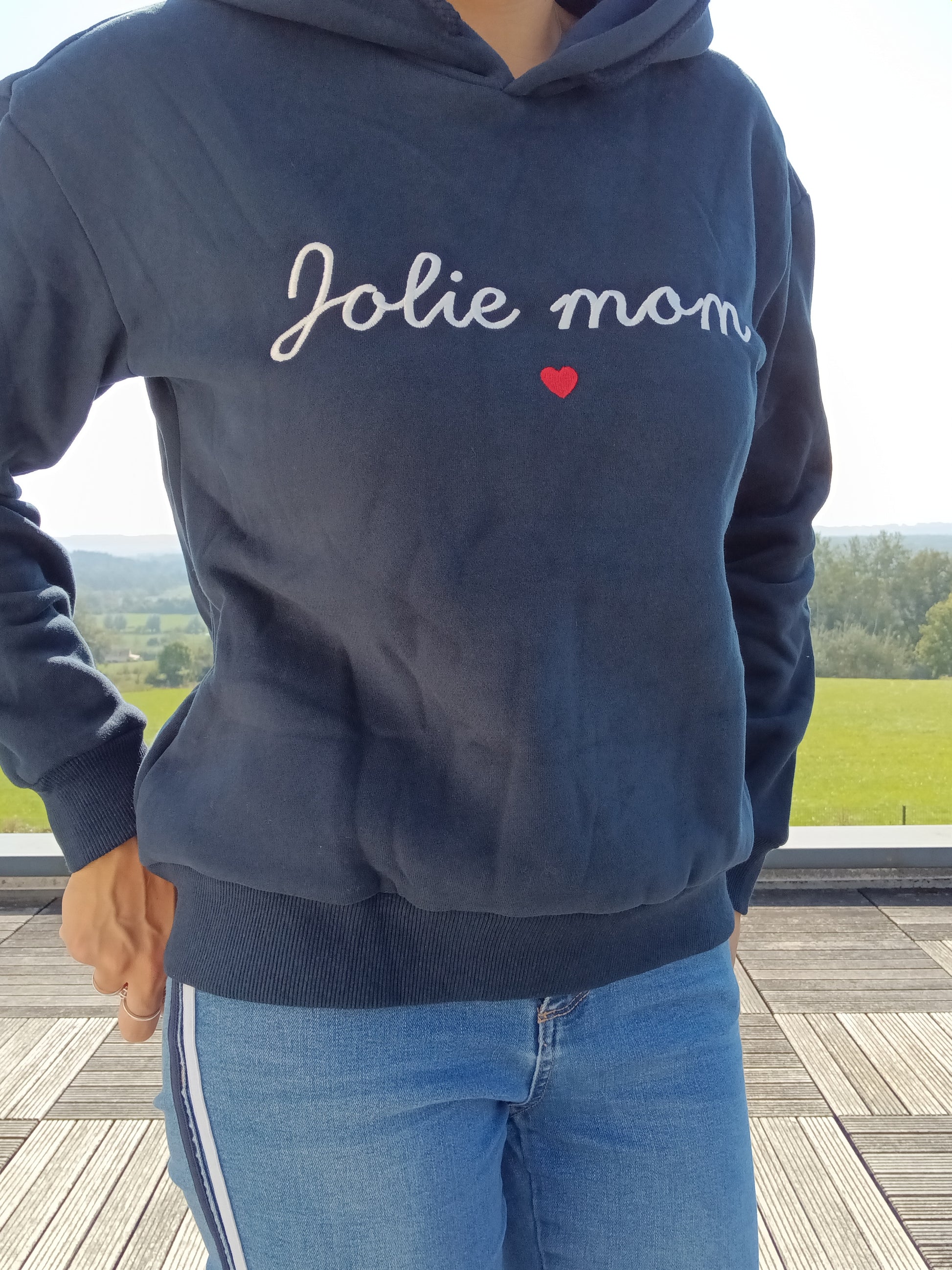 Navy blue hoodie with 'Jolie mom' text and red heart, worn outdoors, Le Petit Placard style.