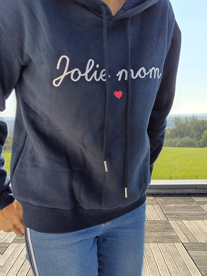 Navy blue hoodie with 'Jolie mom' text and red heart, worn outdoors on a sunny day, Le Petit Placard
