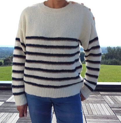 Pull fond blanc double rayures bleu marine et doré avec boutons dorés à l'encolure, porté avec un jean