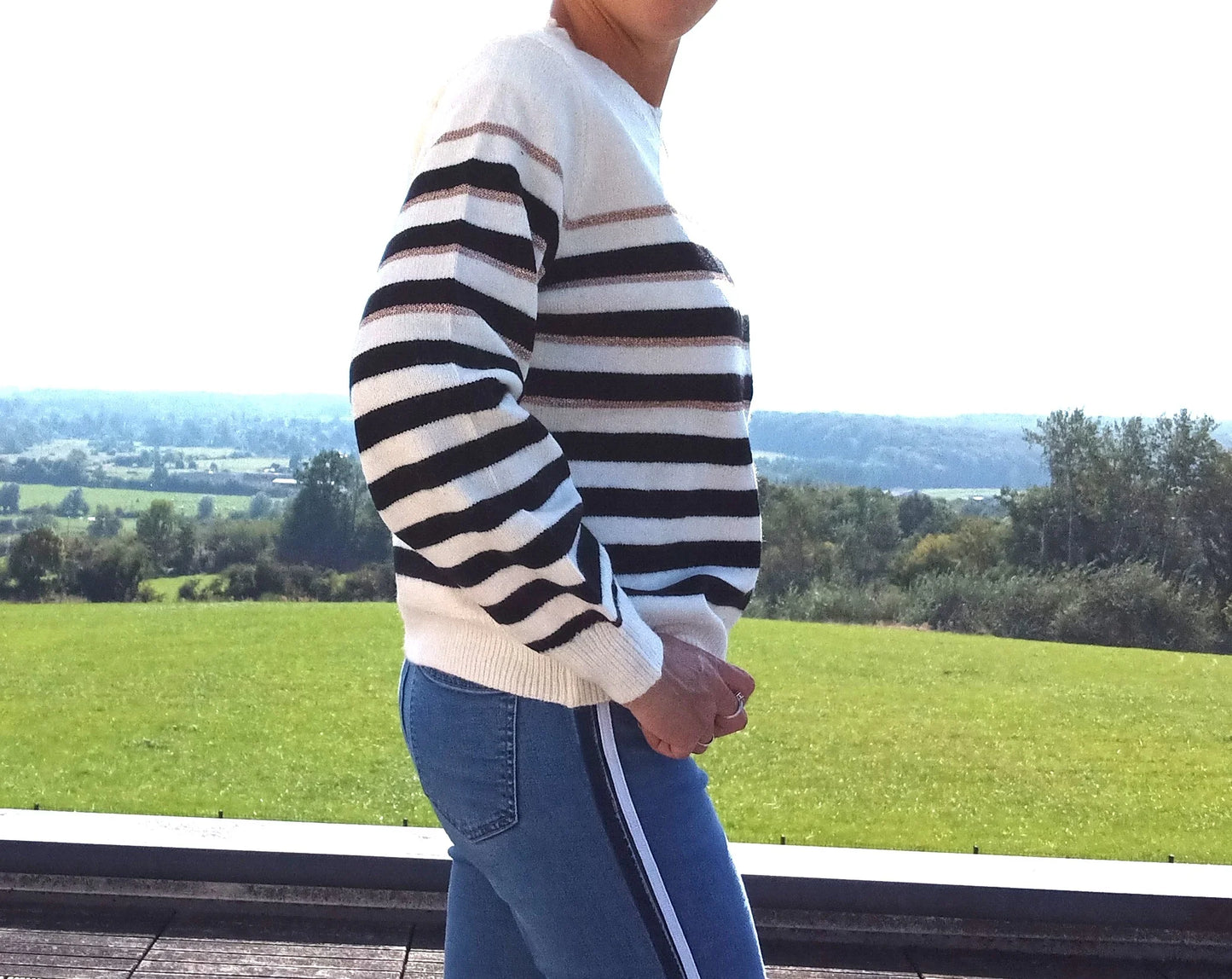 Pull fond blanc larges rayures noires avec fines rayures dorées porté de profil avec un jean, vue extérieure