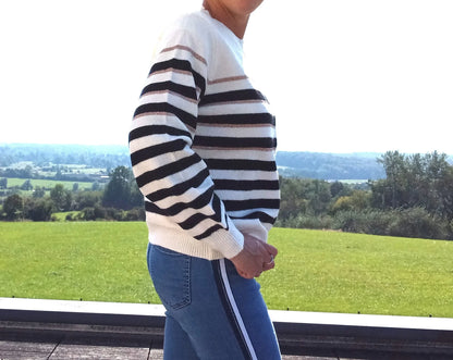 Pull fond blanc larges rayures noires avec fines rayures dorées porté de profil avec un jean, vue extérieure
