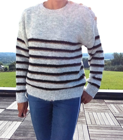 Pull fond gris clair doubles rayures noir et doré porté avec un jean, boutons dorés à l'épaule