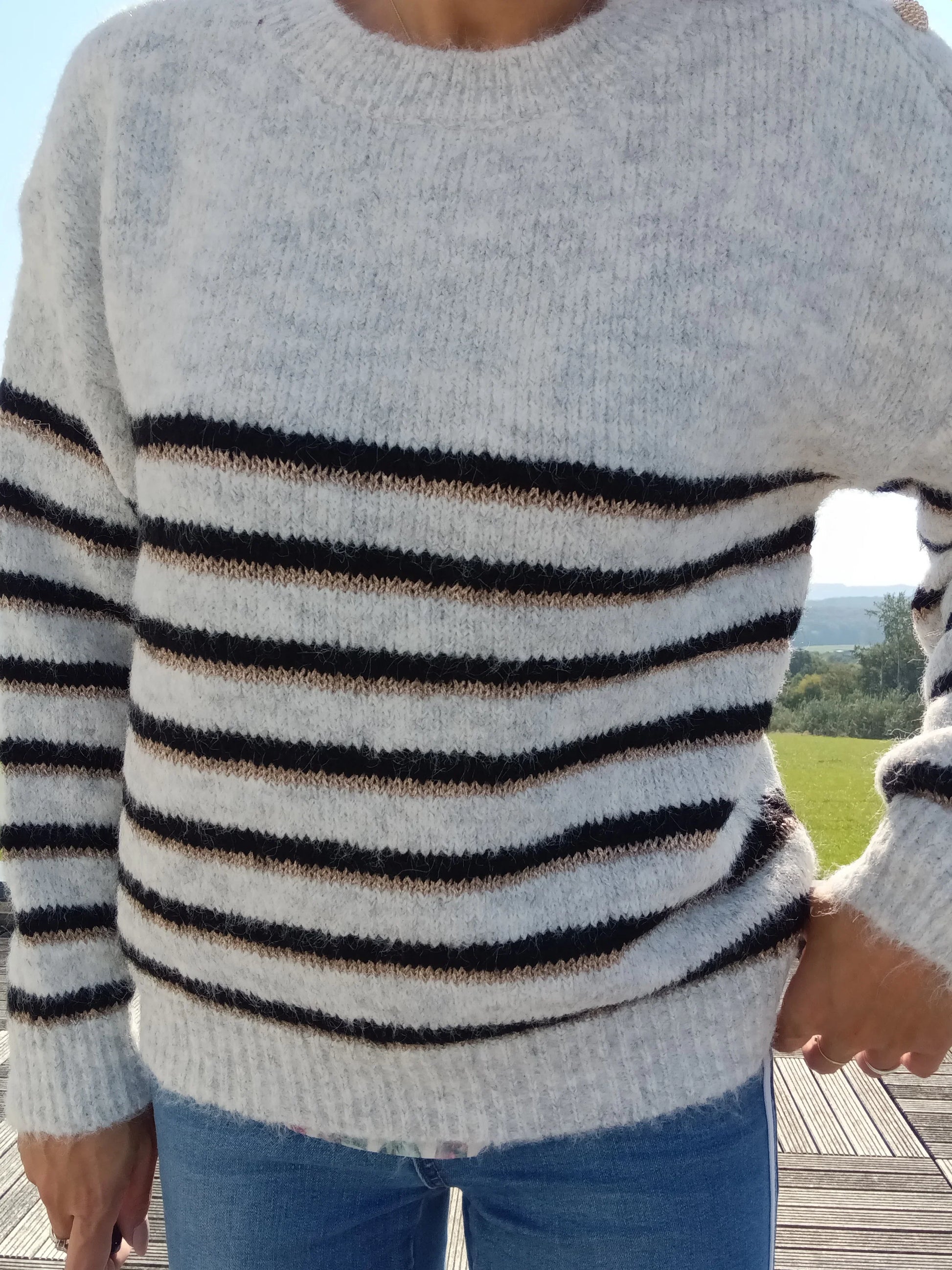 Pull fond gris clair doubles rayures noir et doré porté avec un jean, tricot doux à col rond