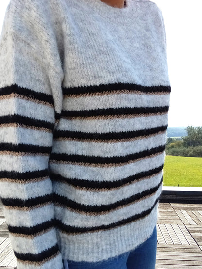 Pull fond gris clair doubles rayures noir et doré porté par une femme, tricot doux et moelleux