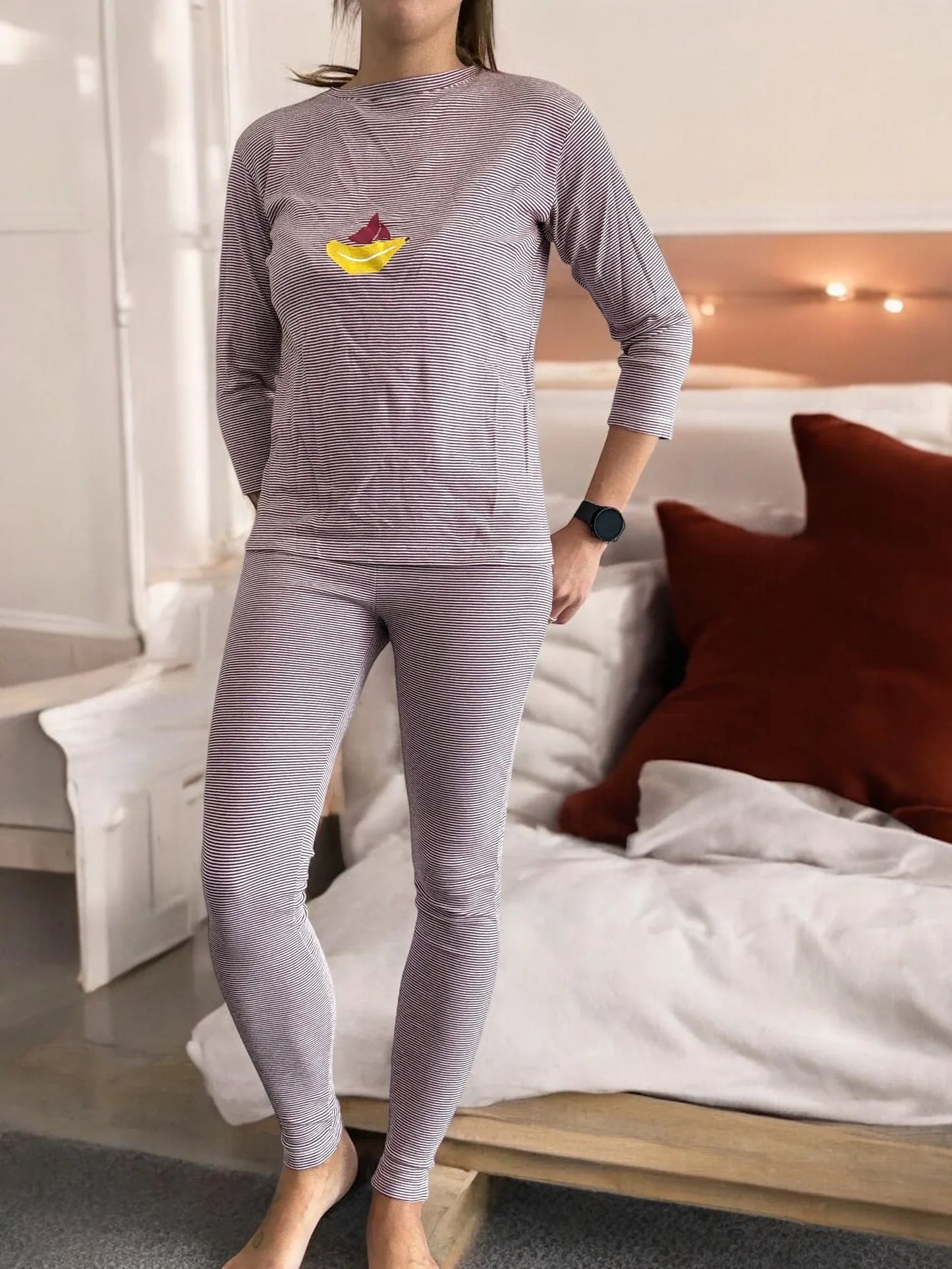 Woman wearing striped pajama set with paper boat design, standing in cozy bedroom by Le Petit Placard