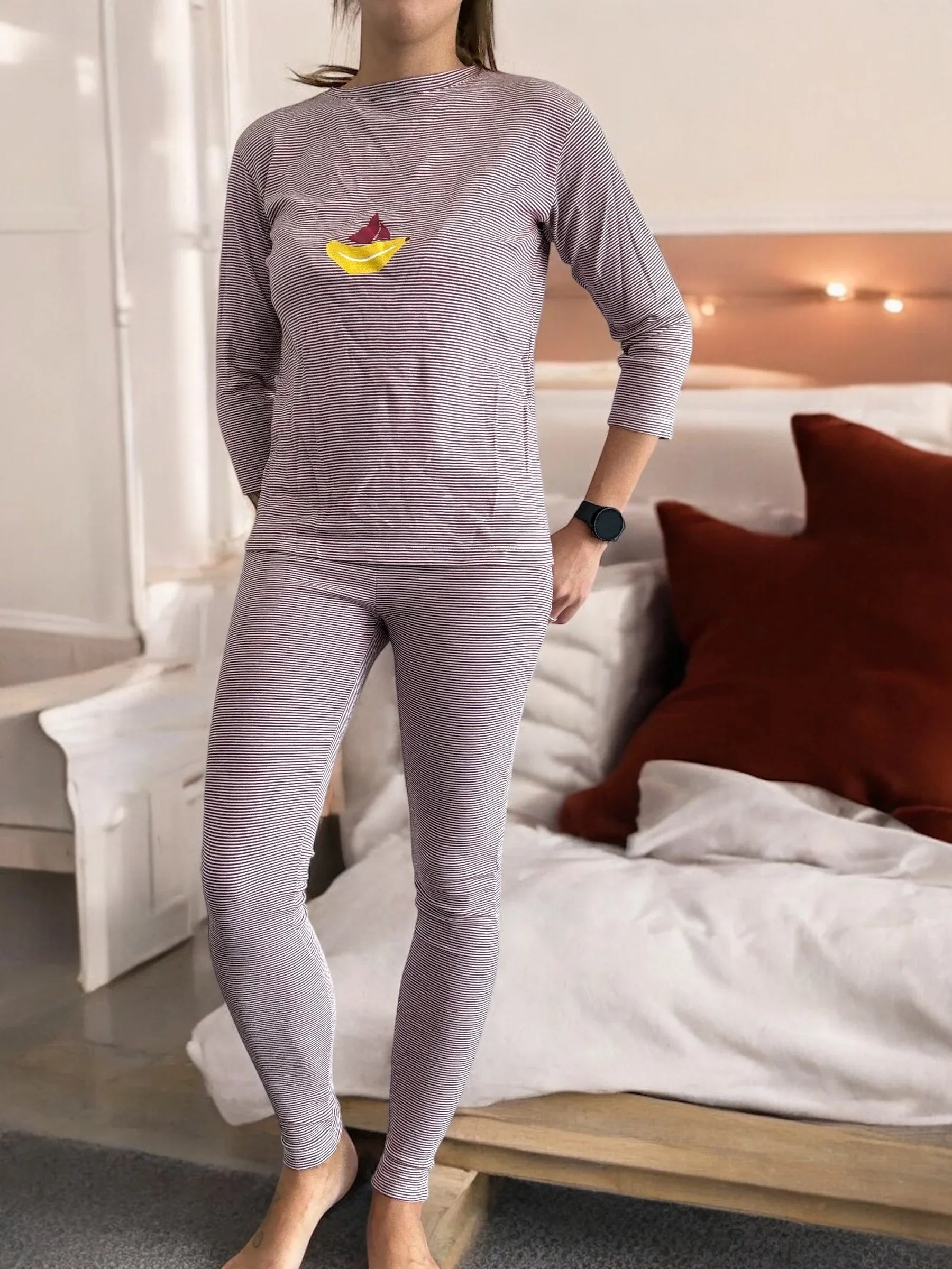 Woman wearing striped pajama set with paper boat design, standing in cozy bedroom by Le Petit Placard