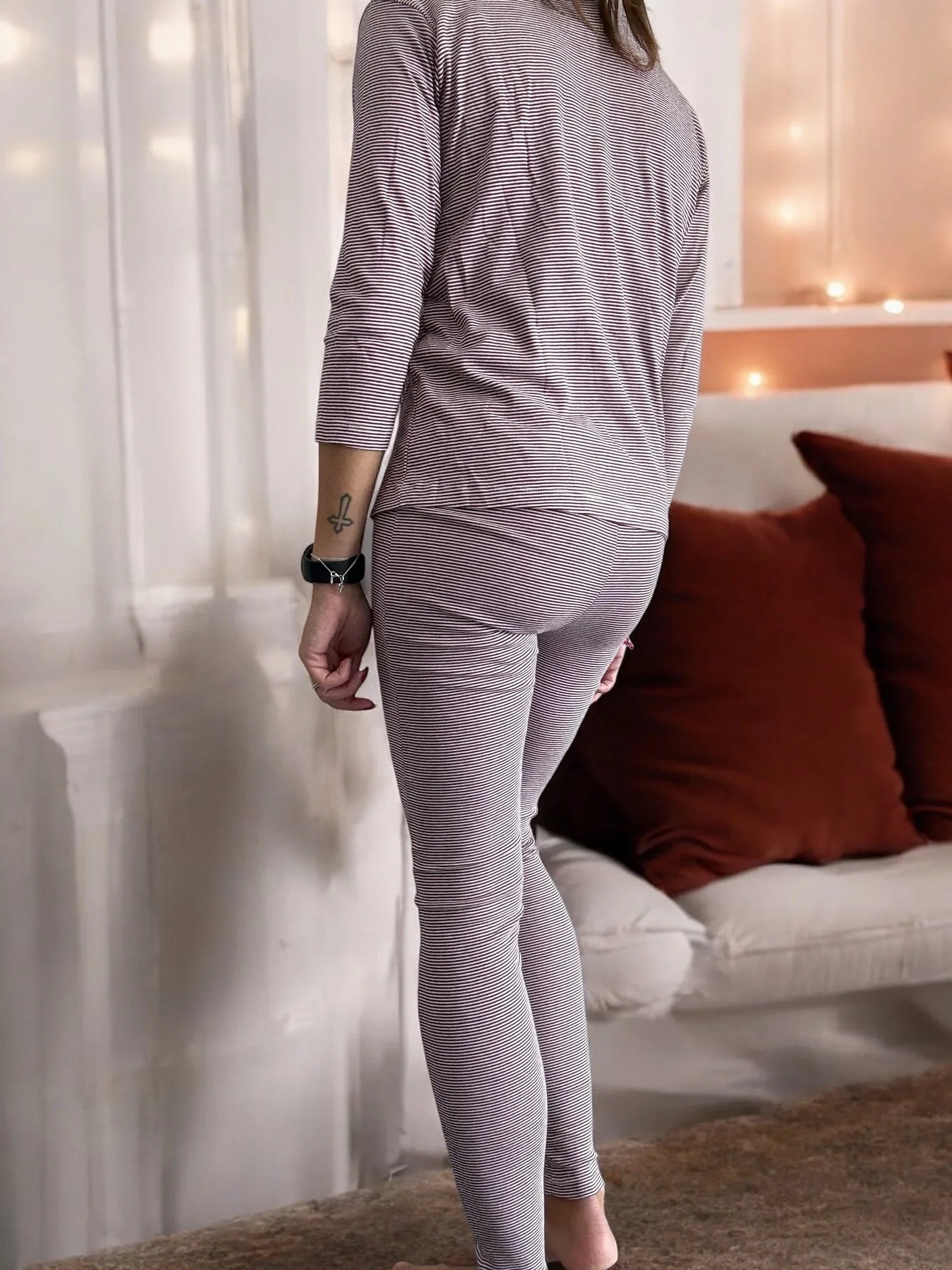 Woman in striped pajamas indoors, cozy setting with neutral decor and brown cushions