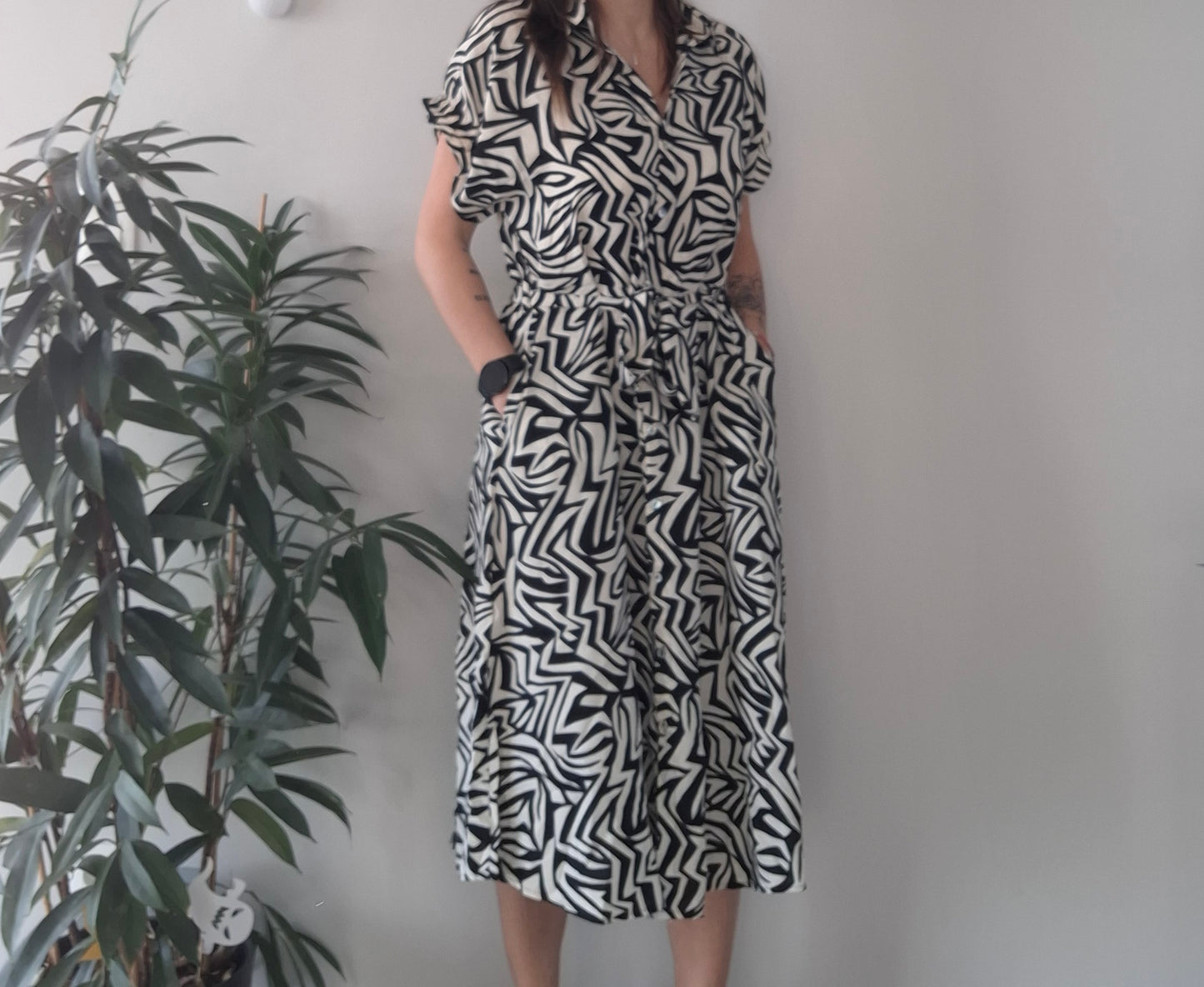 Woman in black and white geometric print dress from Le Petit Placard, standing by indoor plant