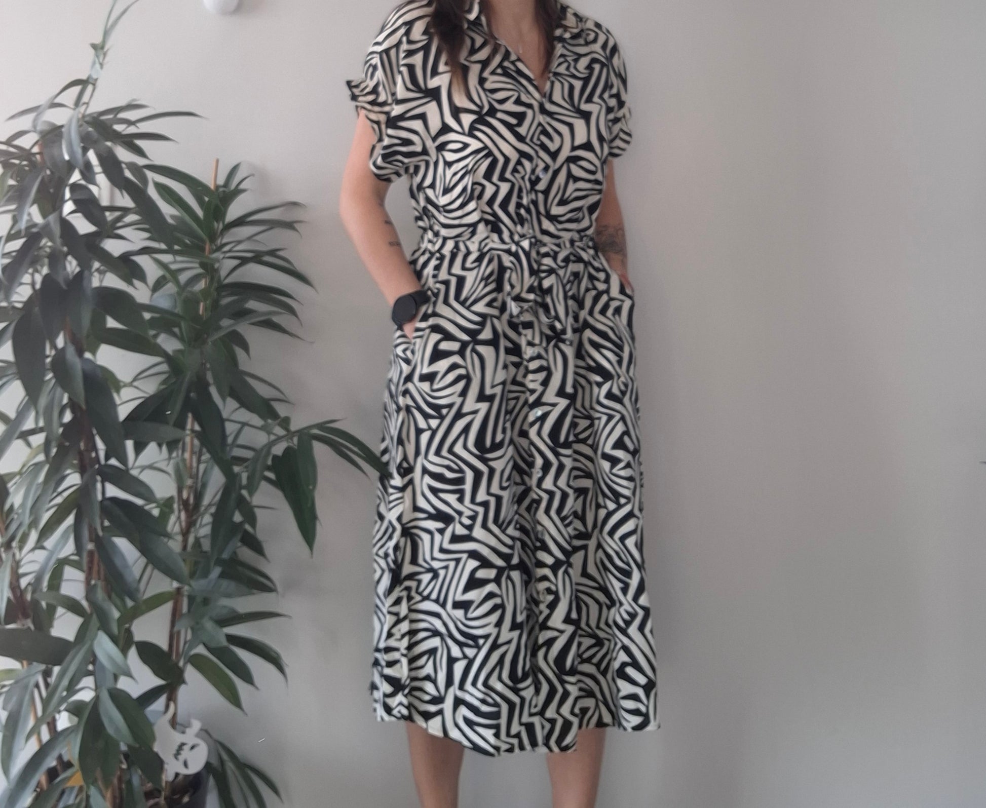 Woman in black and white geometric print dress from Le Petit Placard, standing by indoor plant