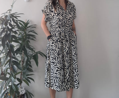 Woman in black and white geometric print dress from Le Petit Placard, standing by indoor plant
