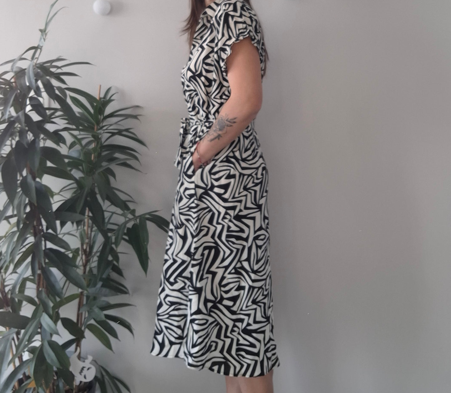 Woman wearing black and white patterned dress, standing near indoor plant, Le Petit Placard