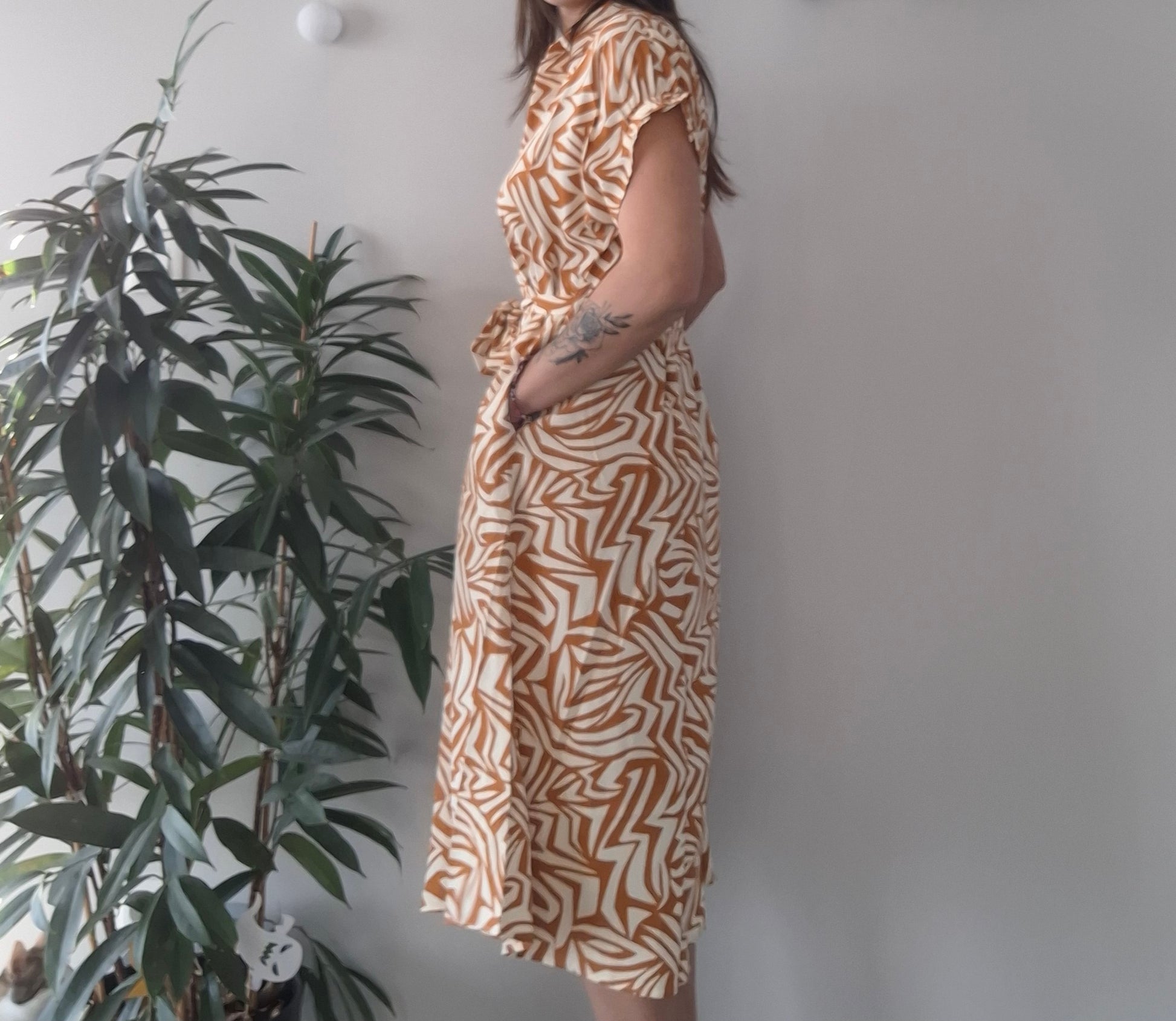 Woman wearing patterned summer dress standing by indoor plant, trendy fashion at Le Petit Placard