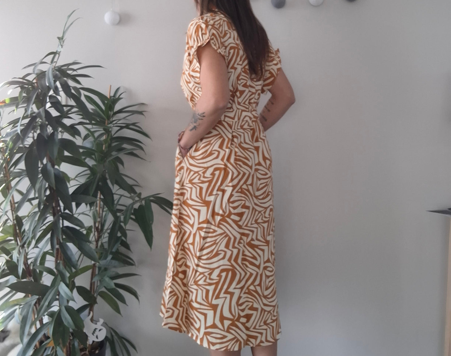 Woman in yellow geometric midi dress standing indoors near a plant, Le Petit Placard fashion