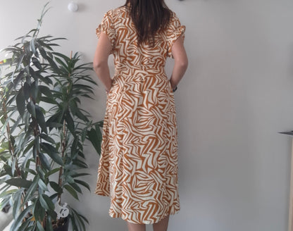 Woman wearing a brown and white geometric print dress, standing indoors near a plant