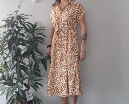 Woman wearing a short-sleeve patterned midi dress from Le Petit Placard, standing indoors
