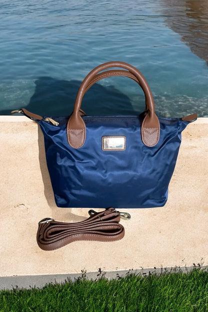 Sac à main fourre-tout petit modèle bleu marine avec anses et bandoulière en cuir marron, posé au bord de l'eau