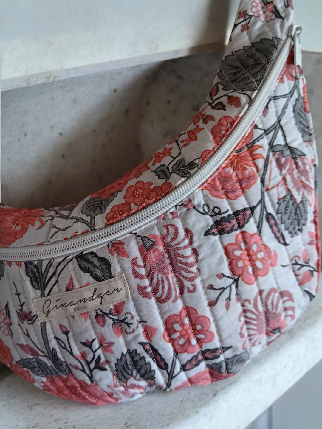 Quilted floral print bum bag with pink and gray flowers, displayed on a white surface.