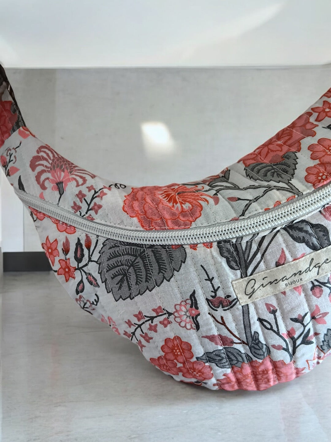 Floral patterned fabric sac banane accessory with zipper, displayed on a light surface