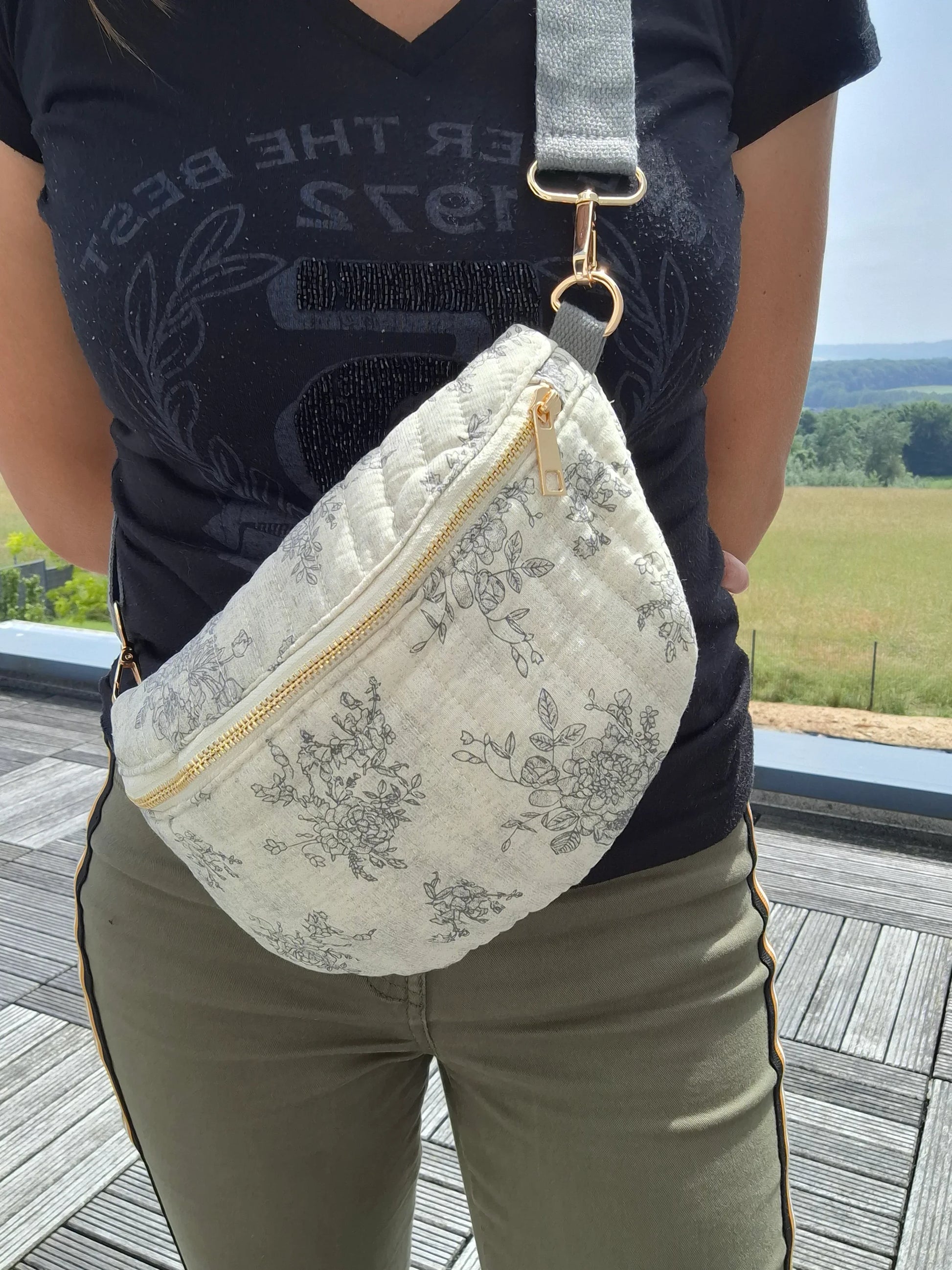 Sac banane en coton matelassé blanc à motif floral gris, zip doré et sangle réglable gris.