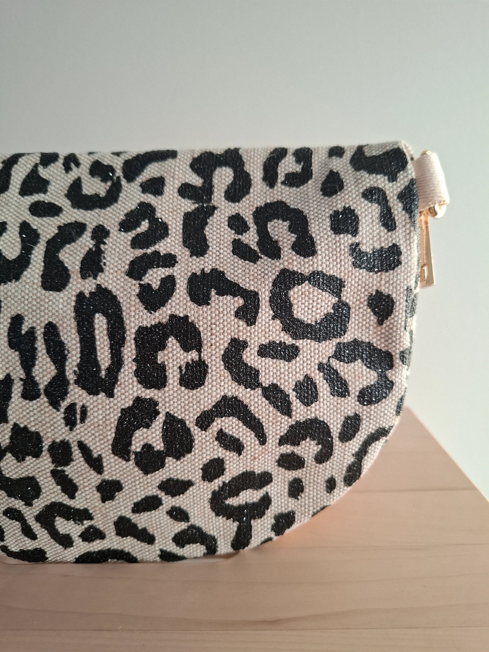 Sac banane motif léopard noir et beige en tissu robuste, avec fermeture éclair dorée, posé sur une surface en bois