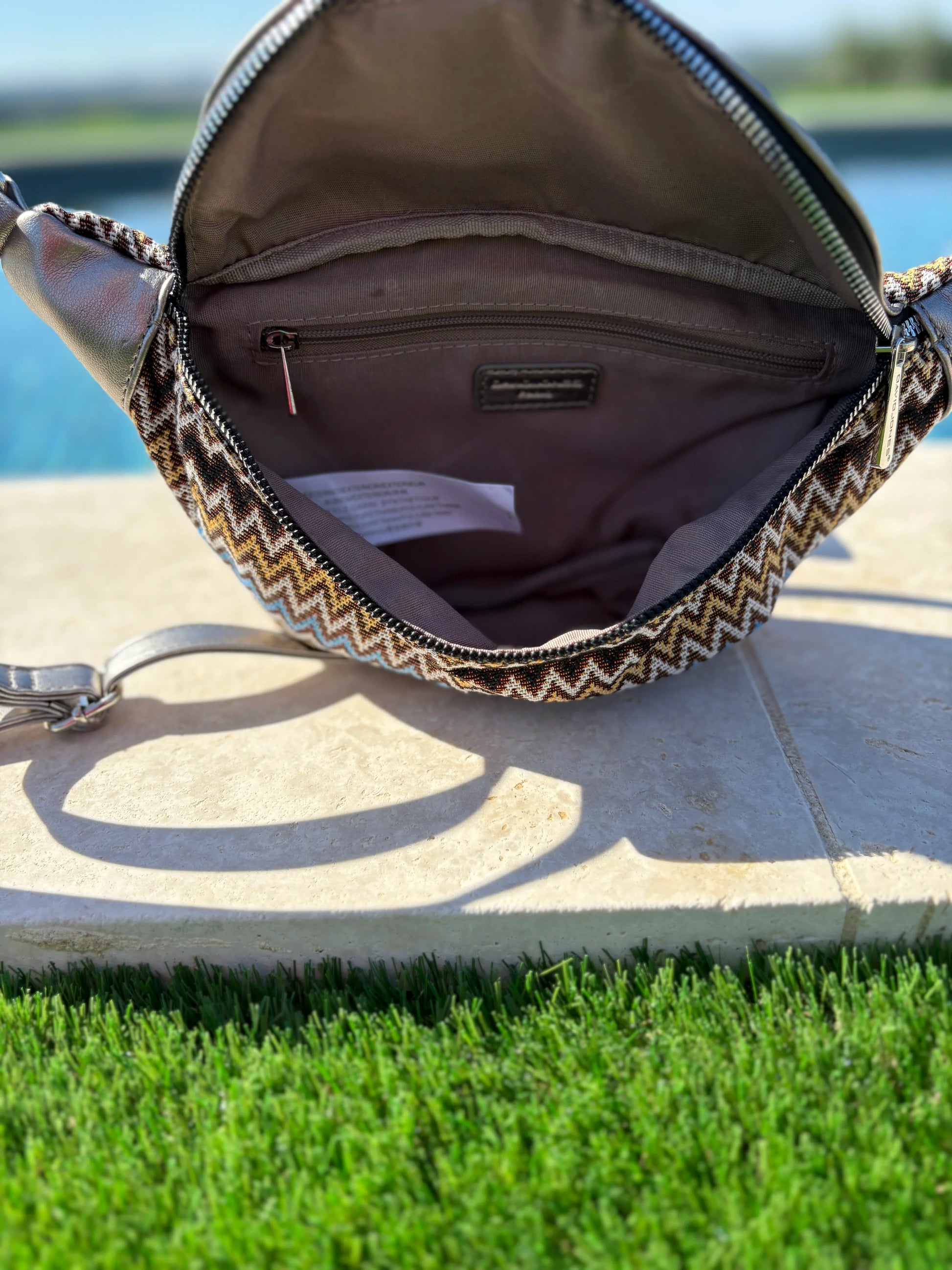 Open chevron-patterned sac banane with interior pocket, photographed outdoors by a pool