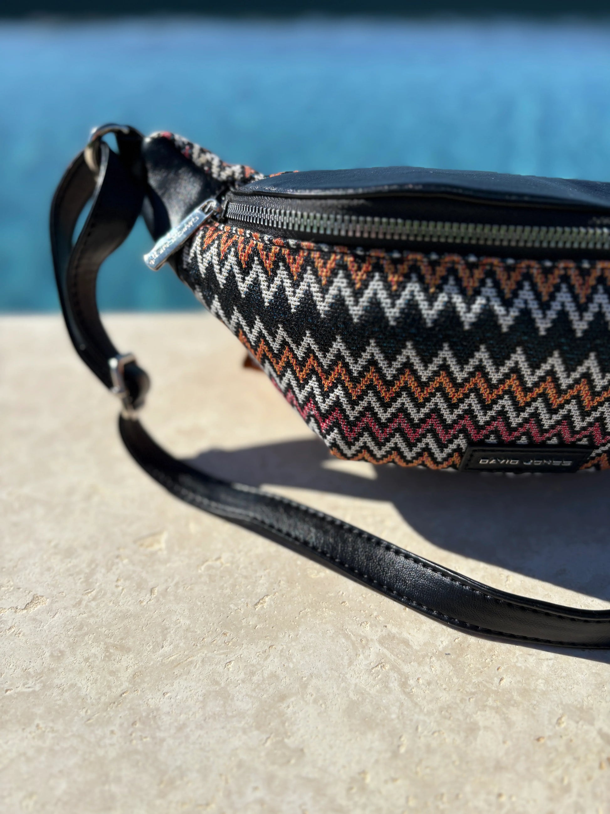Trendy zigzag pattern sac banane by David Jones on stone surface near blue water