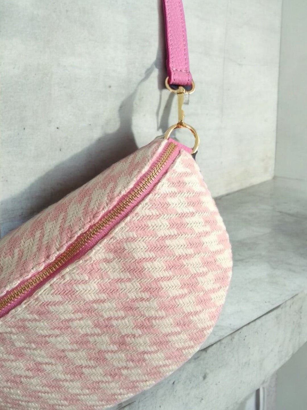 Pink and beige woven sac banane with zigzag pattern and gold zipper on marble surface